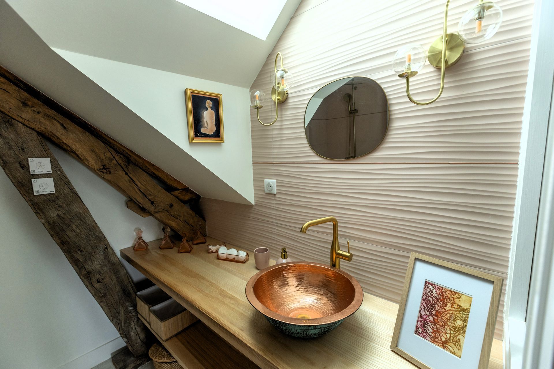 Salle de bain avec lavabo en cuivre, luminaires dorés, comptoir en bois et mur décoratif.