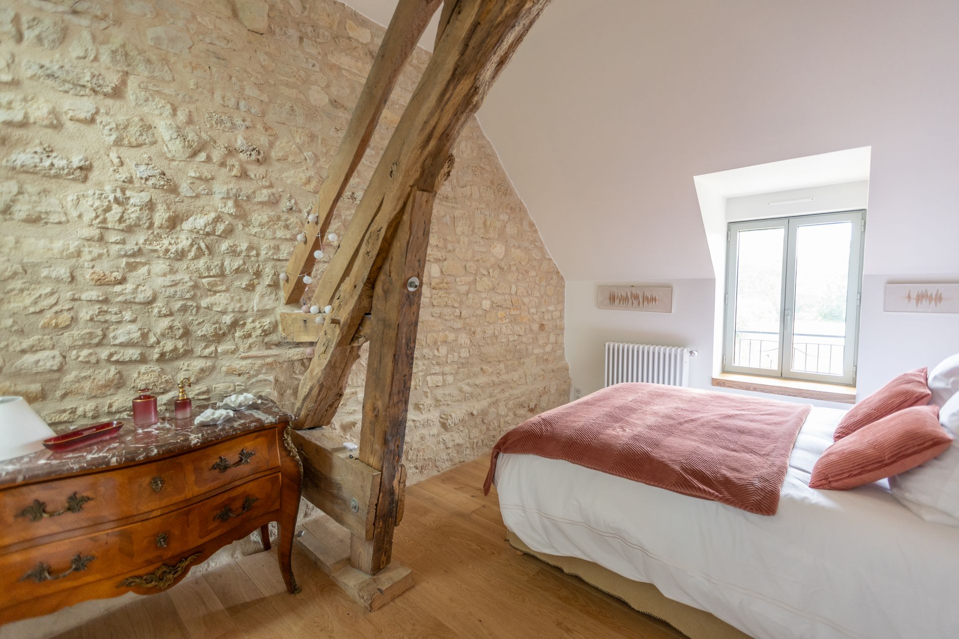 Chambre avec mur en pierres apparentes, poutres en bois et lit avec couverture et oreillers couleur terre cuite.