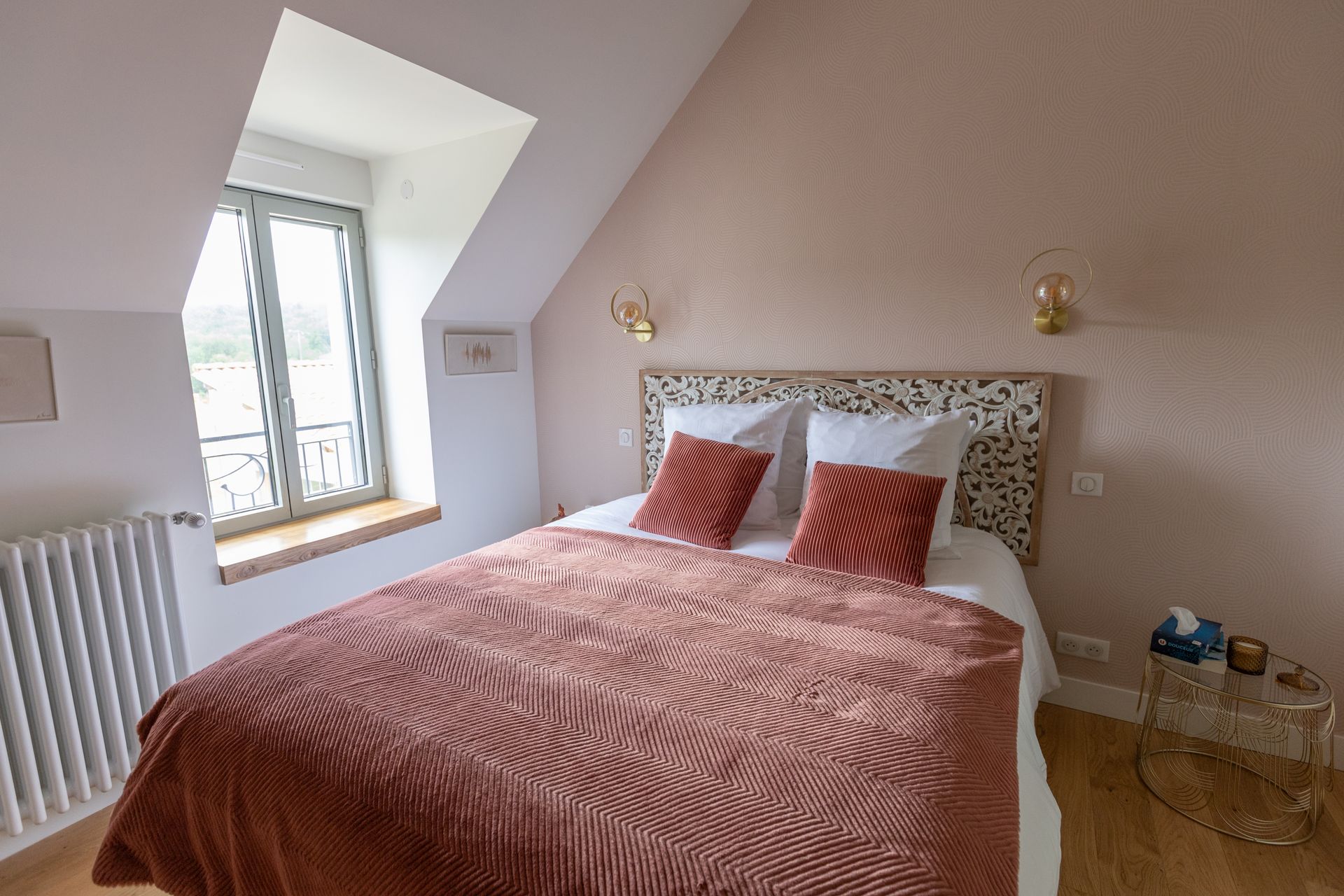 Chambre avec lit, fenêtre et appliques murales ; murs rose blush, tête de lit neutre.