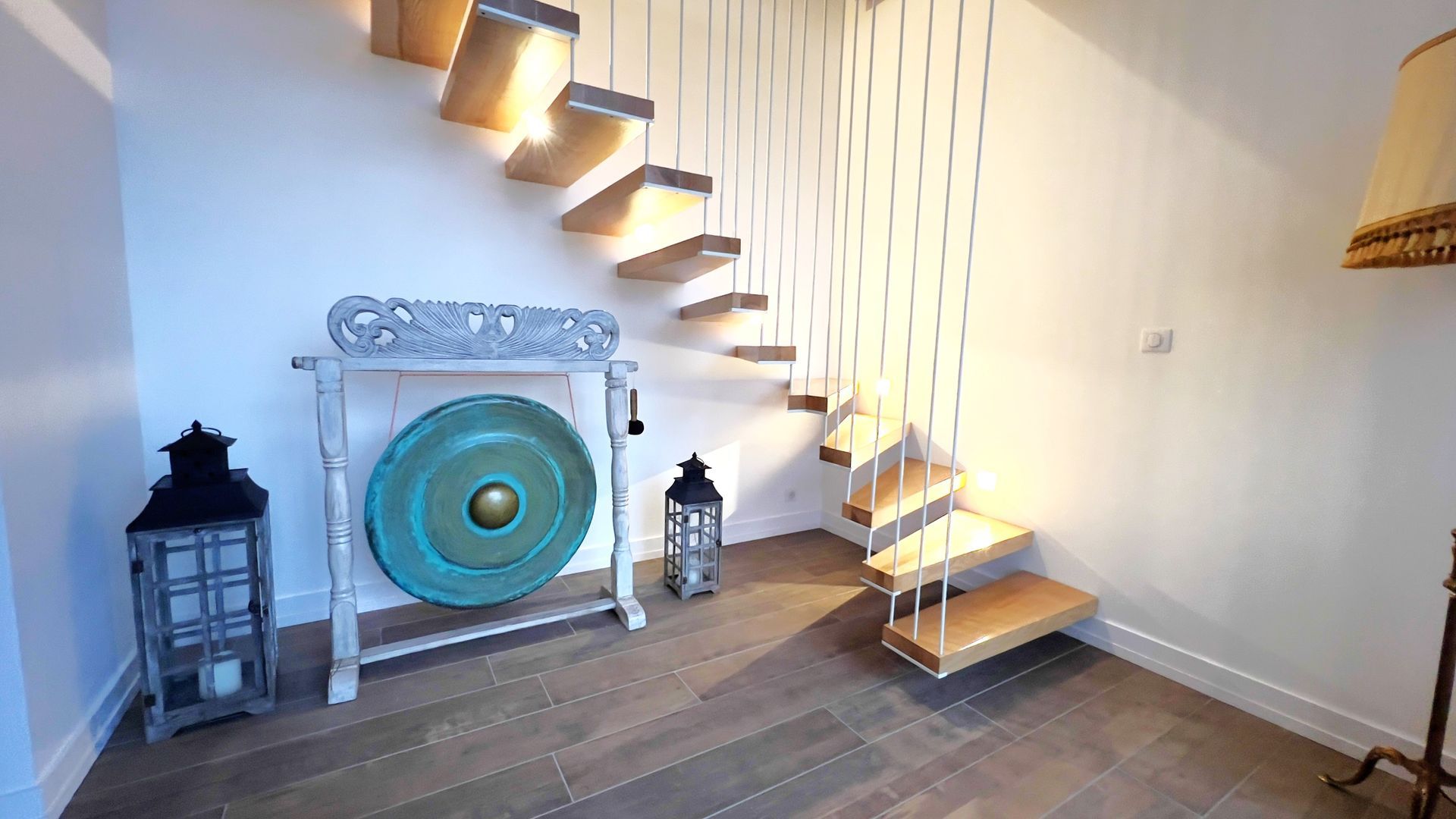 Un gong en bronze et des lanternes sous un escalier flottant.