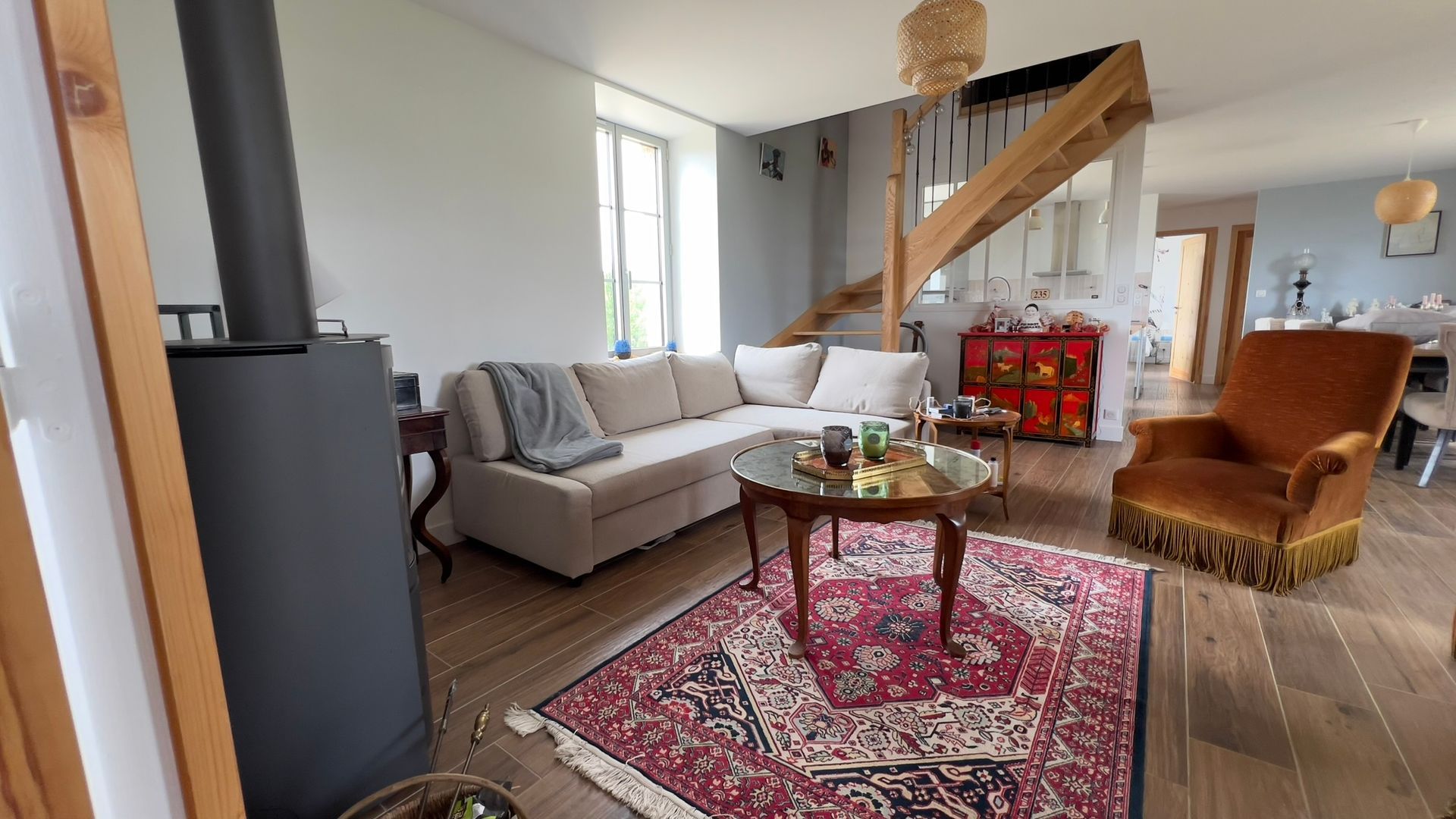 Salon avec un canapé, un tapis rouge, une cheminée et un fauteuil en velours orange.