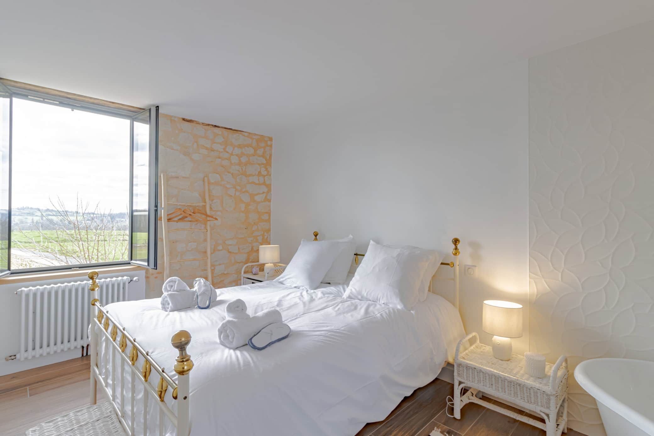 Chambre blanche avec un lit, une table de chevet et une grande fenêtre offrant une vue.