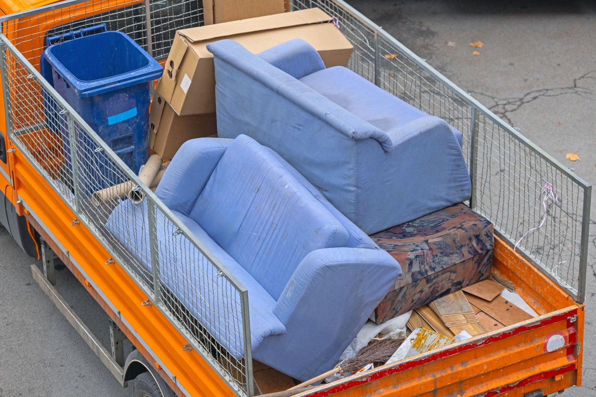 Orange truck bed with blue couches, boxes, trash bin, and debris, possibly for disposal.