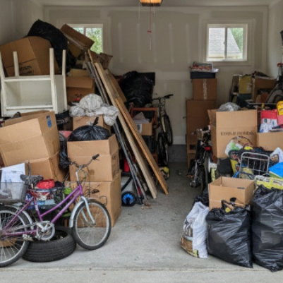 Cluttered garage filled with boxes, bikes, bags, and various items.