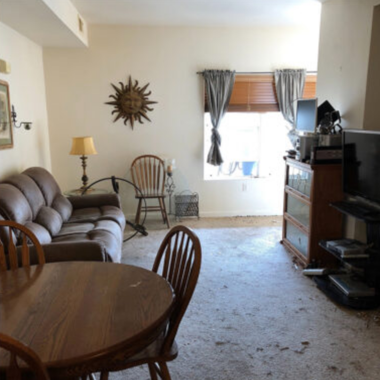 Living room with brown sofa, round wooden table, and sunburst wall decor.