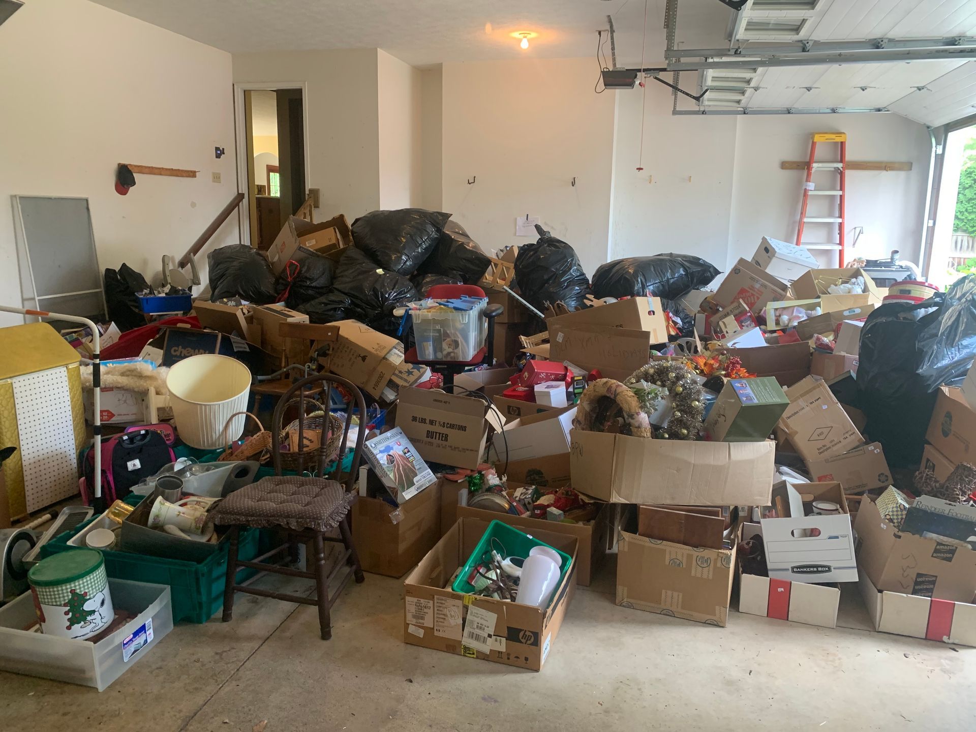 Cluttered garage filled with boxes, bags, and various items. Door and doorway visible.