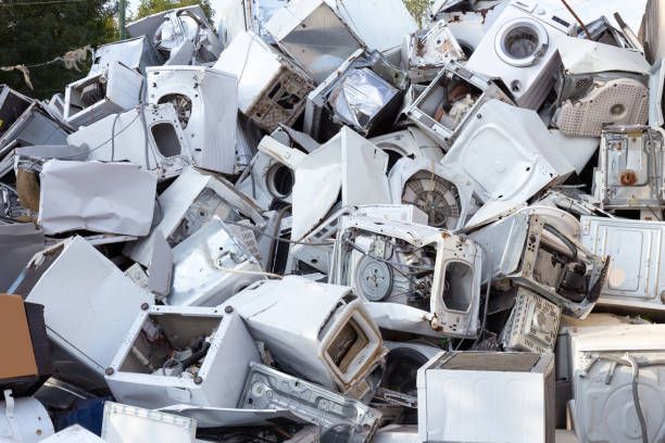 Pile of discarded white appliances, including washing machines and dryers.