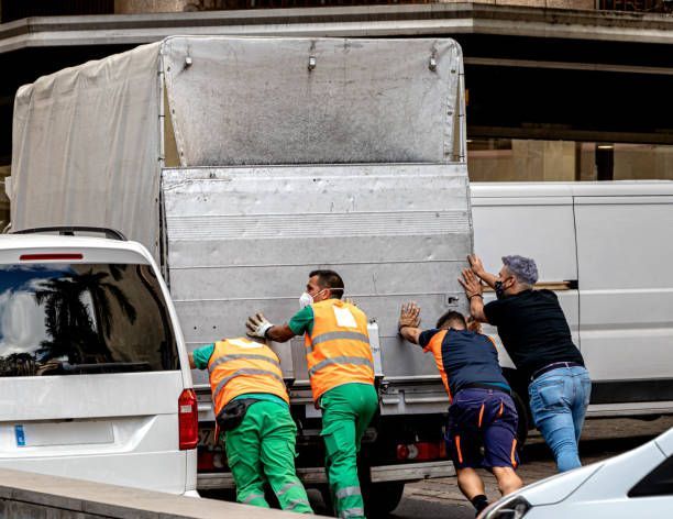 Four people pushing a white truck in an urban setting.