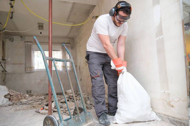 A person wearing a mask loads debris into a trash truck in an urban setting.