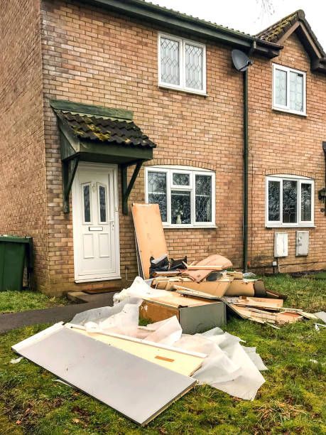 Pile of discarded construction materials in front of a brick house with white windows and door.