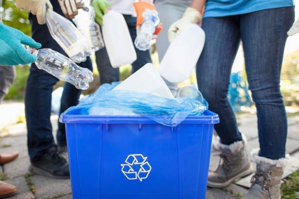 People in gloves putting plastic bottles into a blue recycling bin.