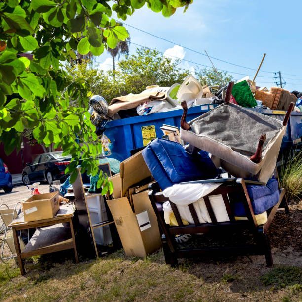 Overflowing blue dumpster with furniture and debris on a sunny day.