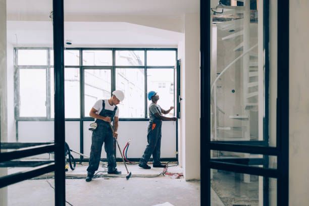 Three people in red jumpsuits hold cleaning tools inside a building.