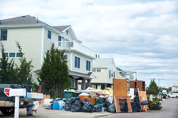 Hand holding keys in front of a miniature wooden house, suggesting home ownership.