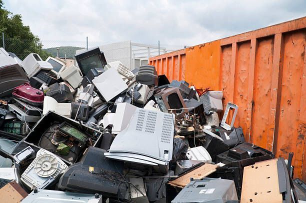 Pile of old televisions and computer monitors in an orange dumpster.