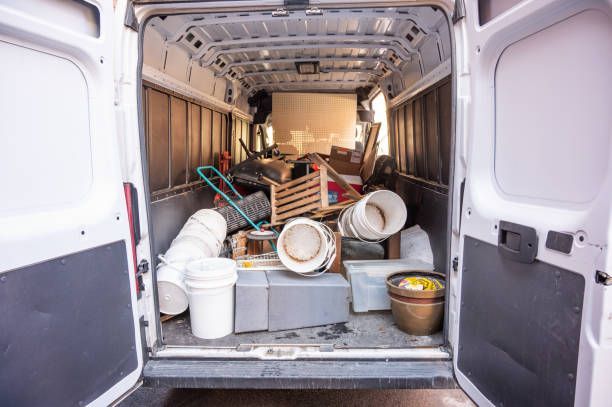 Open back of a white van filled with various debris, including buckets, pallets, and trash.