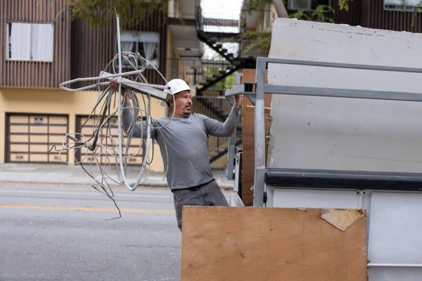 Person picking up trash, placing a cup into a black garbage bag in a field.