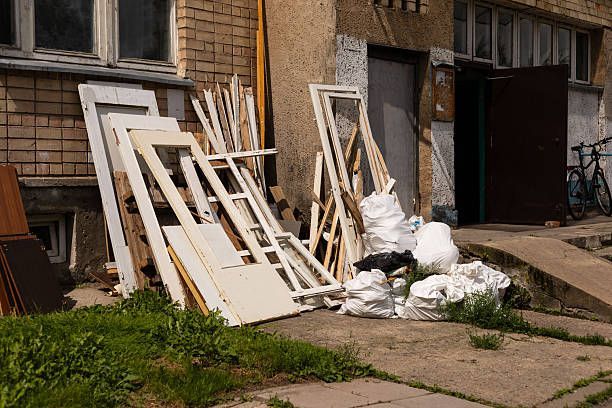 Exterior view of a building with construction debris: doors, wood, and bags piled up near the entrance and grass.