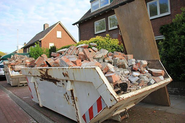 A dumpster overflowing with brick rubble, parked on a street near a house.