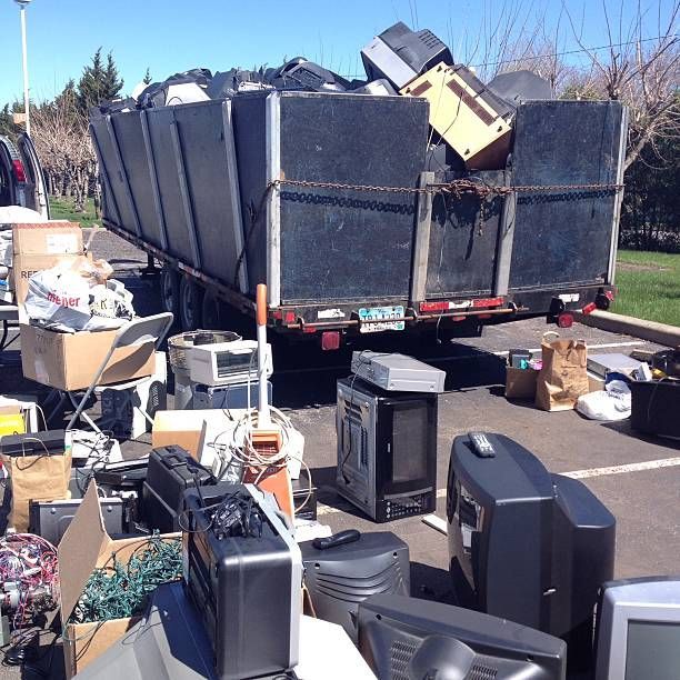 A dumpster overflowing with discarded electronics and appliances in a parking lot.