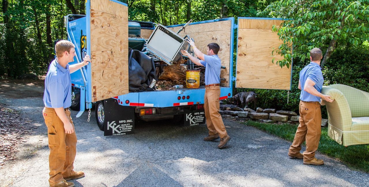 Three movers loading furniture and appliances into a blue truck in a driveway.