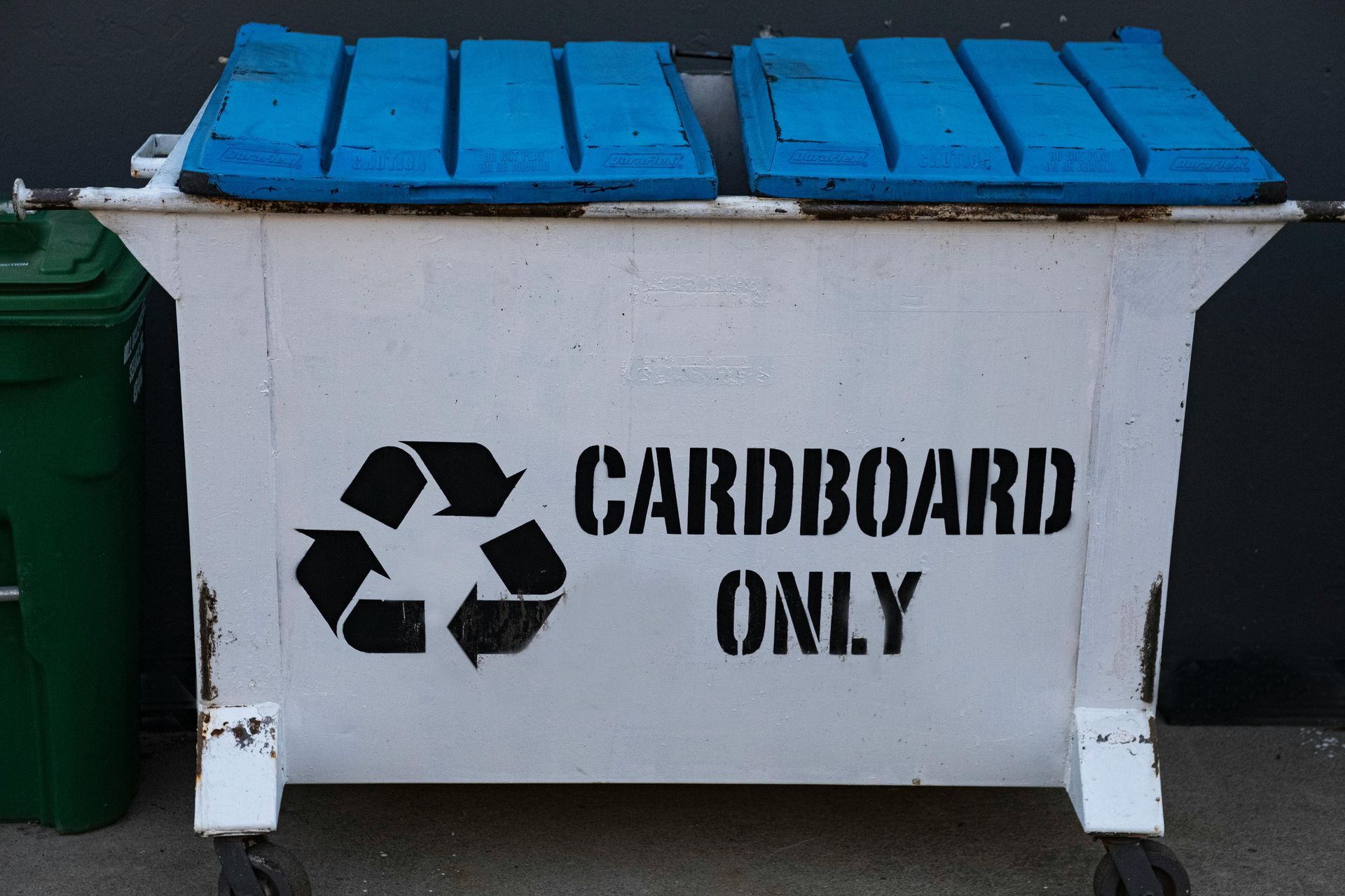 White cardboard recycling dumpster with blue lids and a green bin.