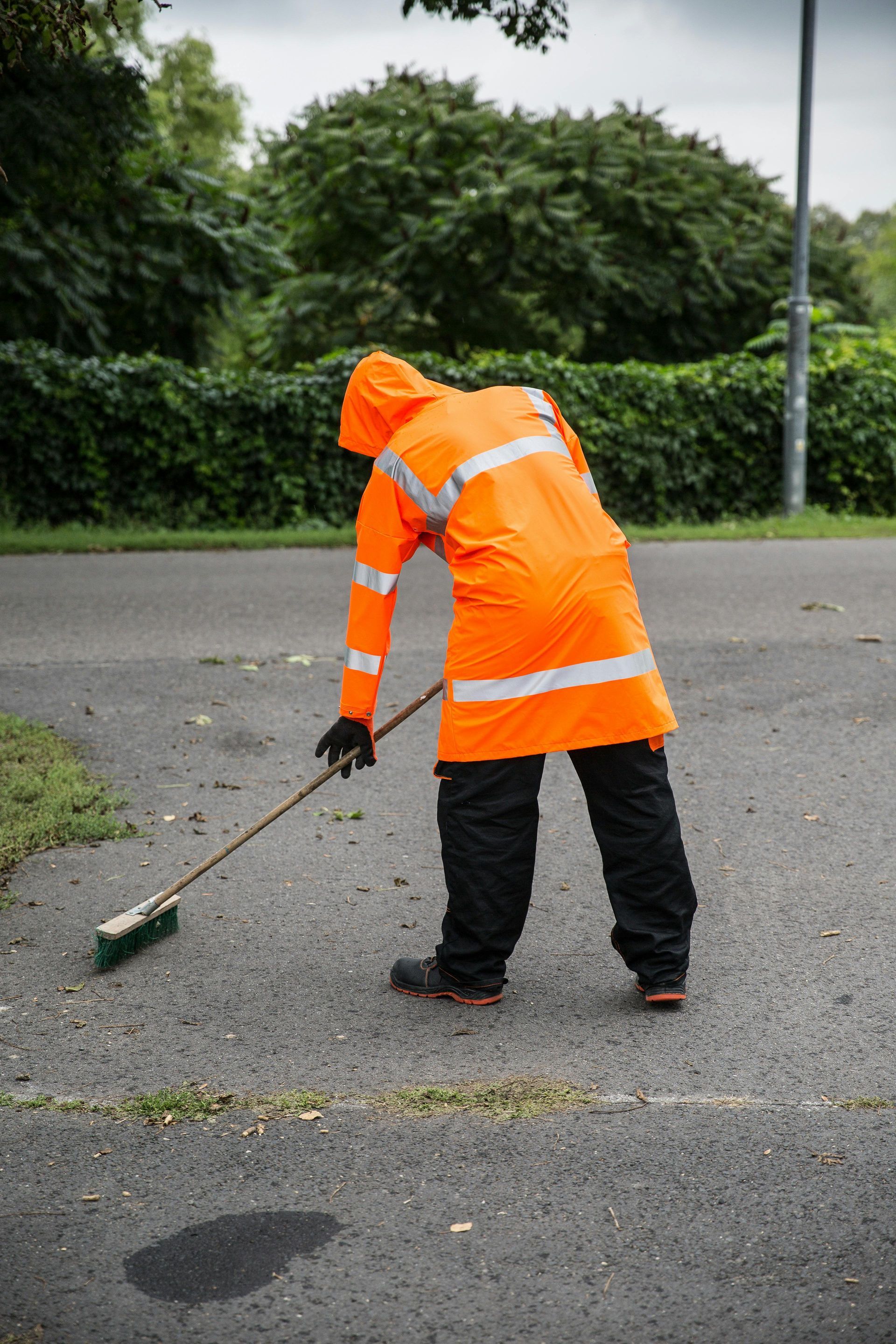 Person in orange reflective gear sweeping asphalt road.