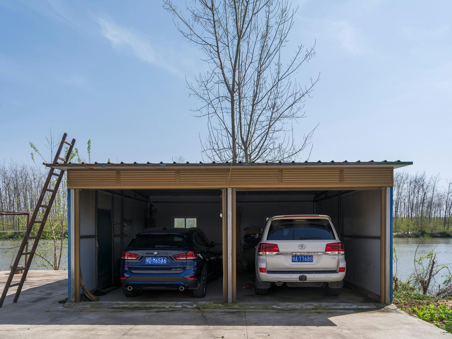 Two cars parked in a dual-bay garage, next to water and a ladder on the side.