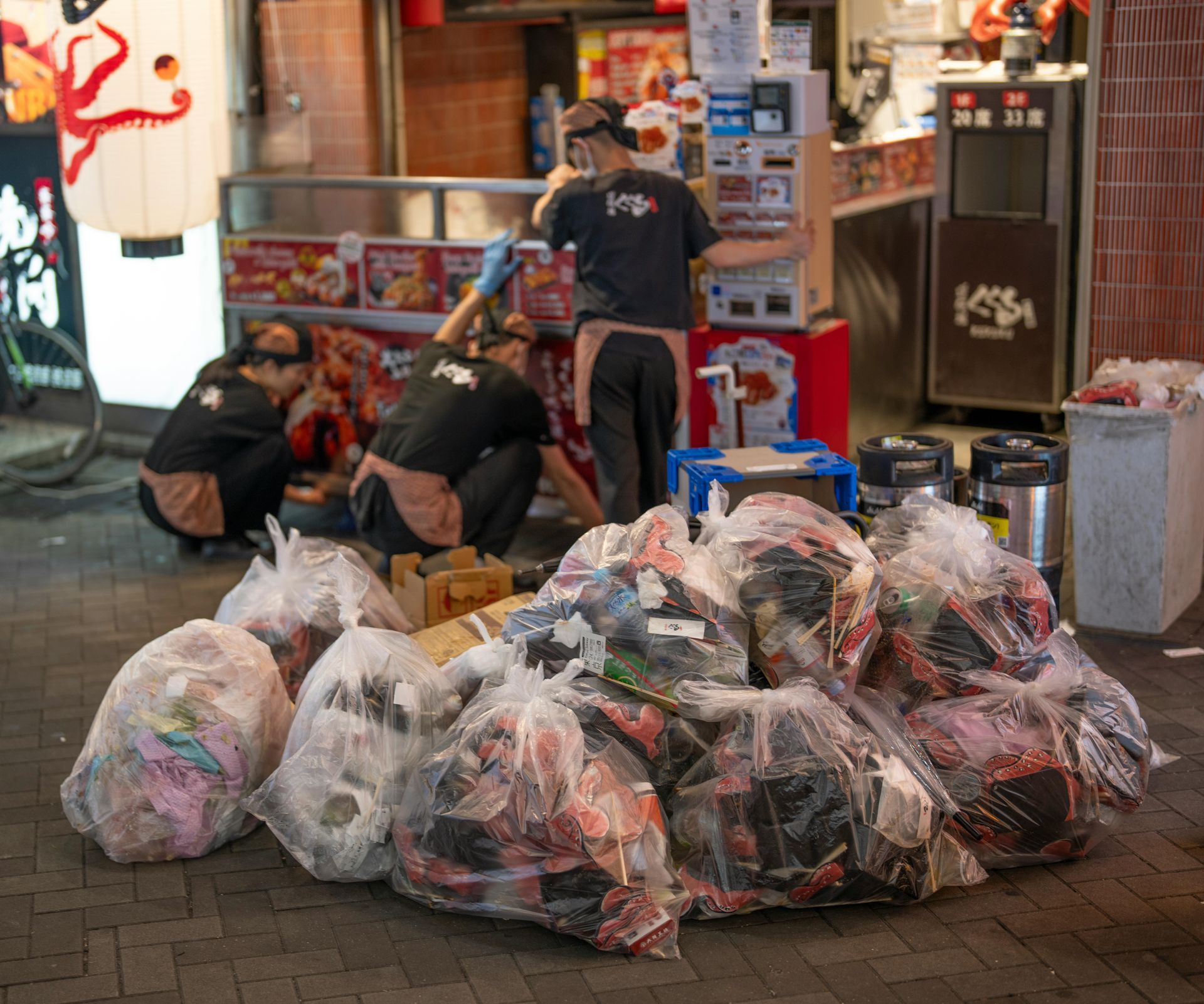 People near a Japanese restaurant, sorting trash bags.