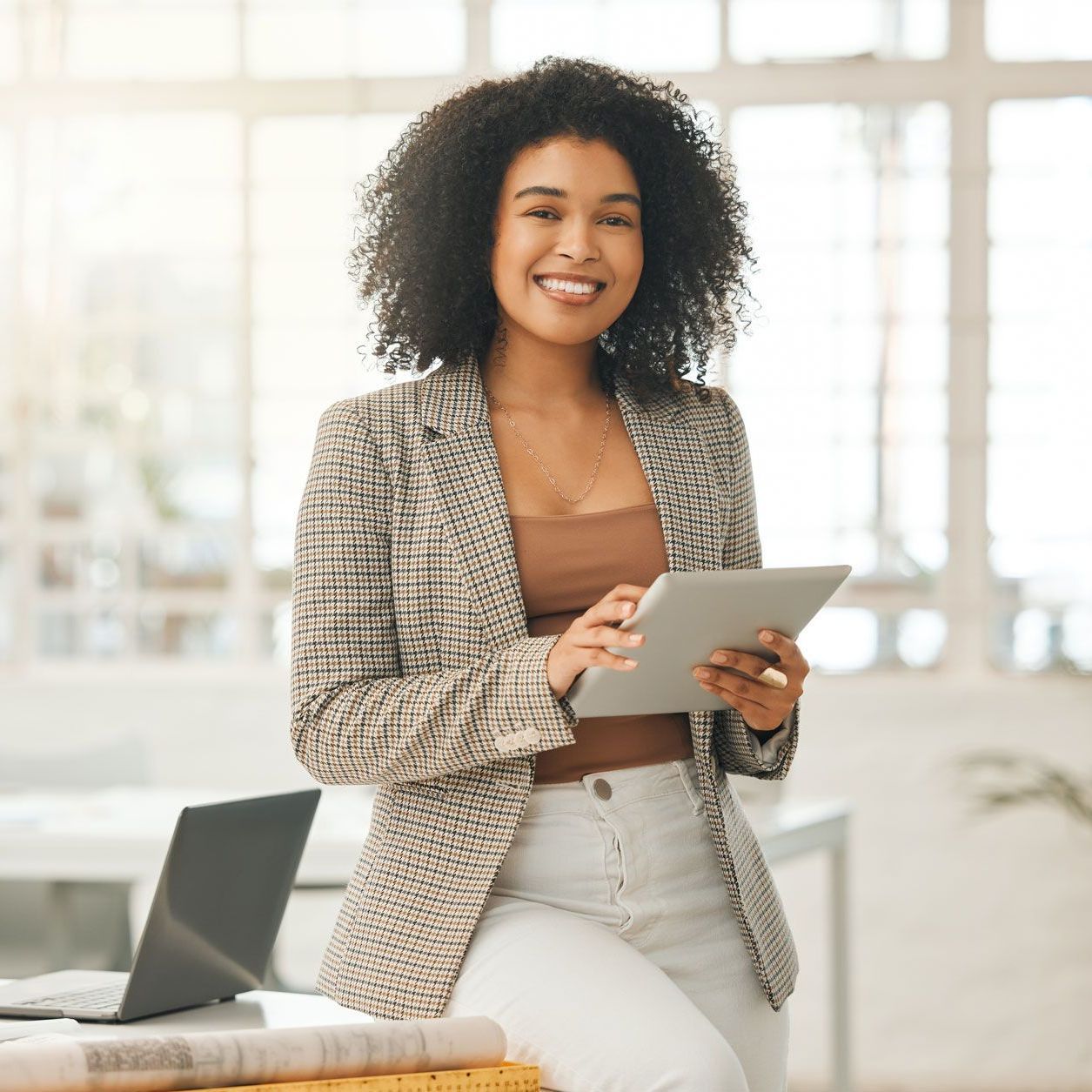 A woman is sitting at a desk holding a tablet computer.