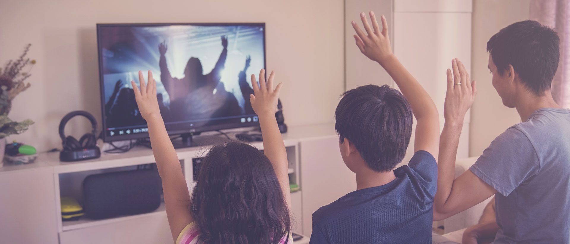 A family is sitting in front of a television with their hands in the air.