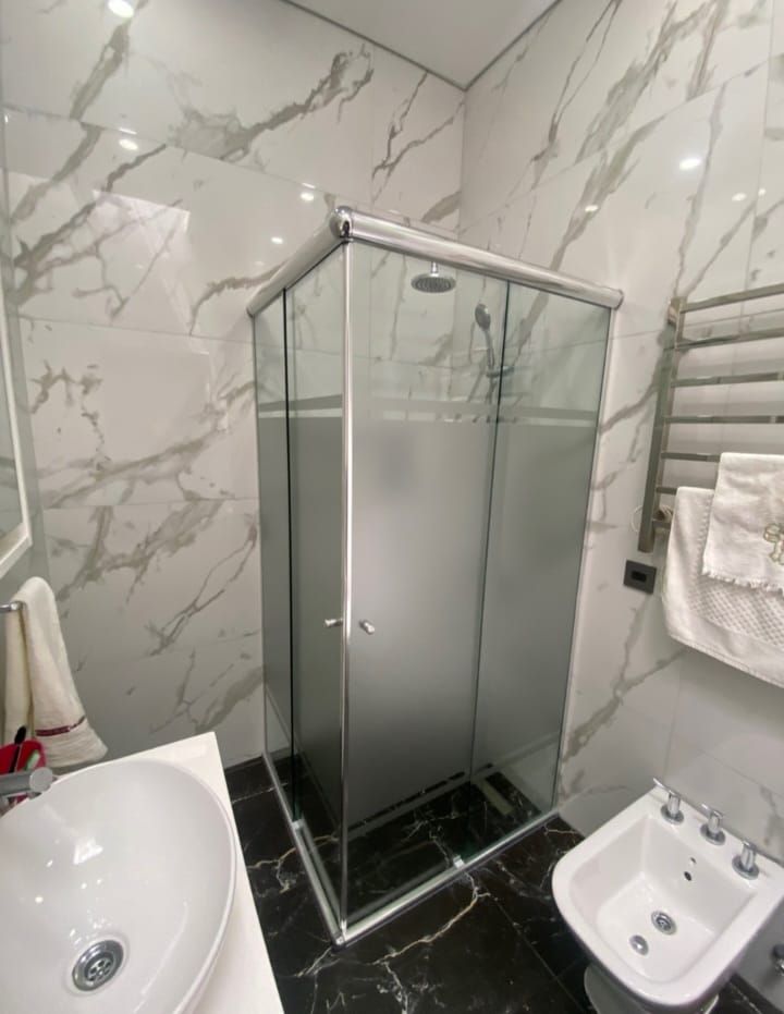 Baño moderno con ducha de cristal, lavabo blanco, bidé y paredes con estampado de mármol.