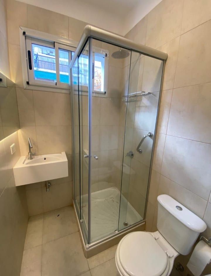 Baño con ducha, inodoro y lavabo; paredes de azulejos beige; ventana pequeña.