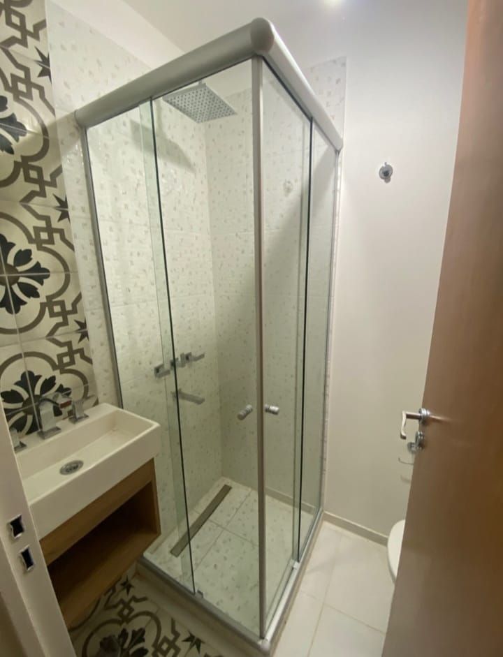 Baño con ducha de cristal, lavabo y azulejos decorativos. La ducha está cerrada con marco cromado.