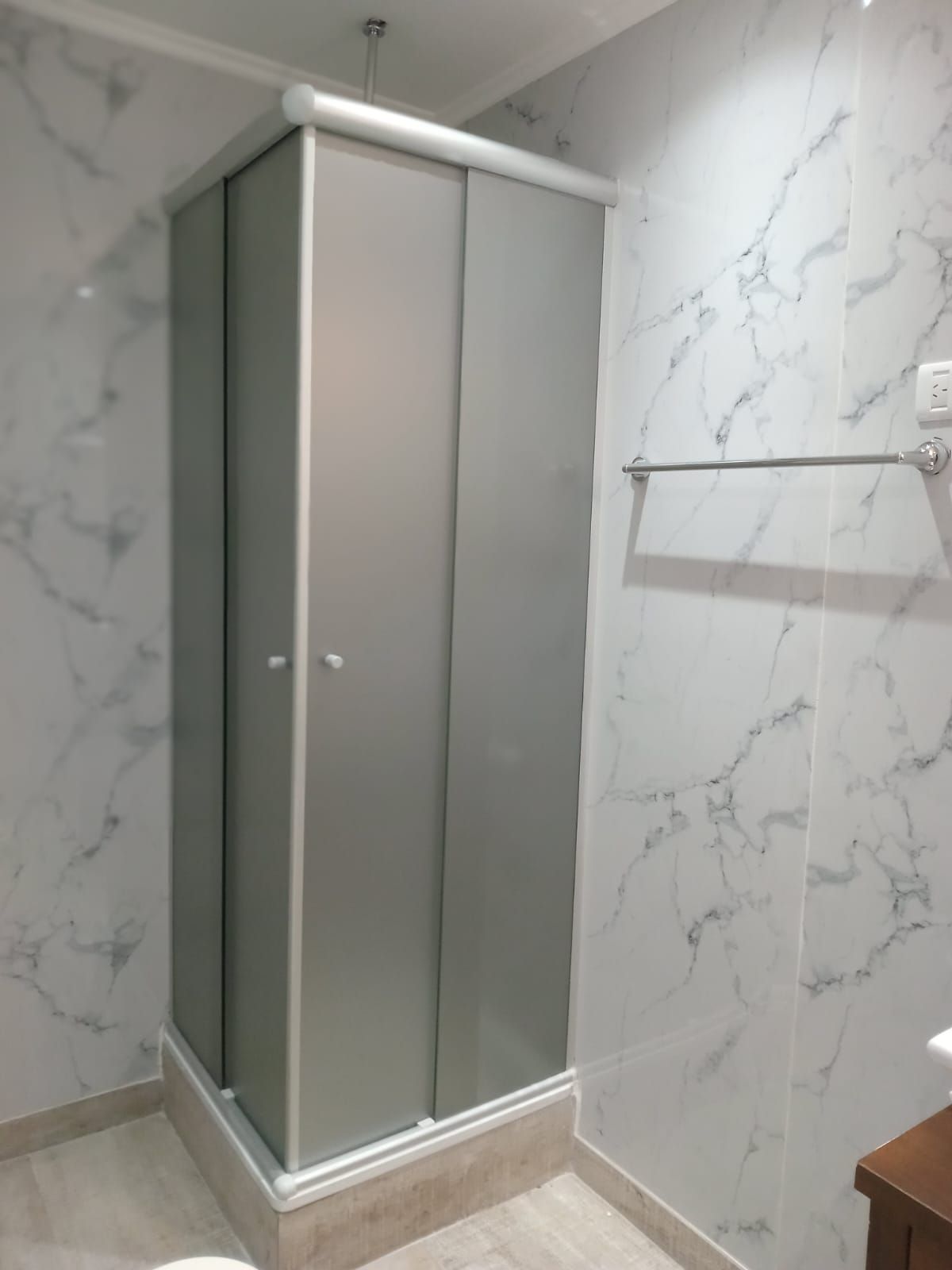 Mampara de ducha con puertas correderas en un baño con paredes con estampado de mármol.