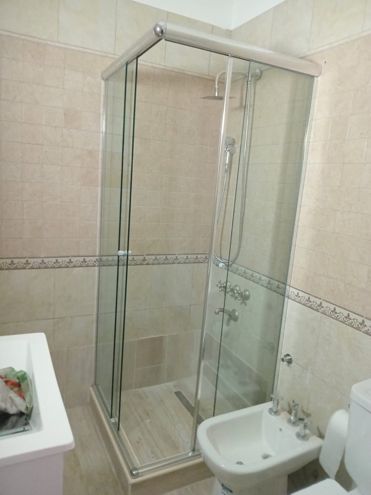 Cabina de ducha con puertas de cristal, junto a bidé e inodoro en baño alicatado.