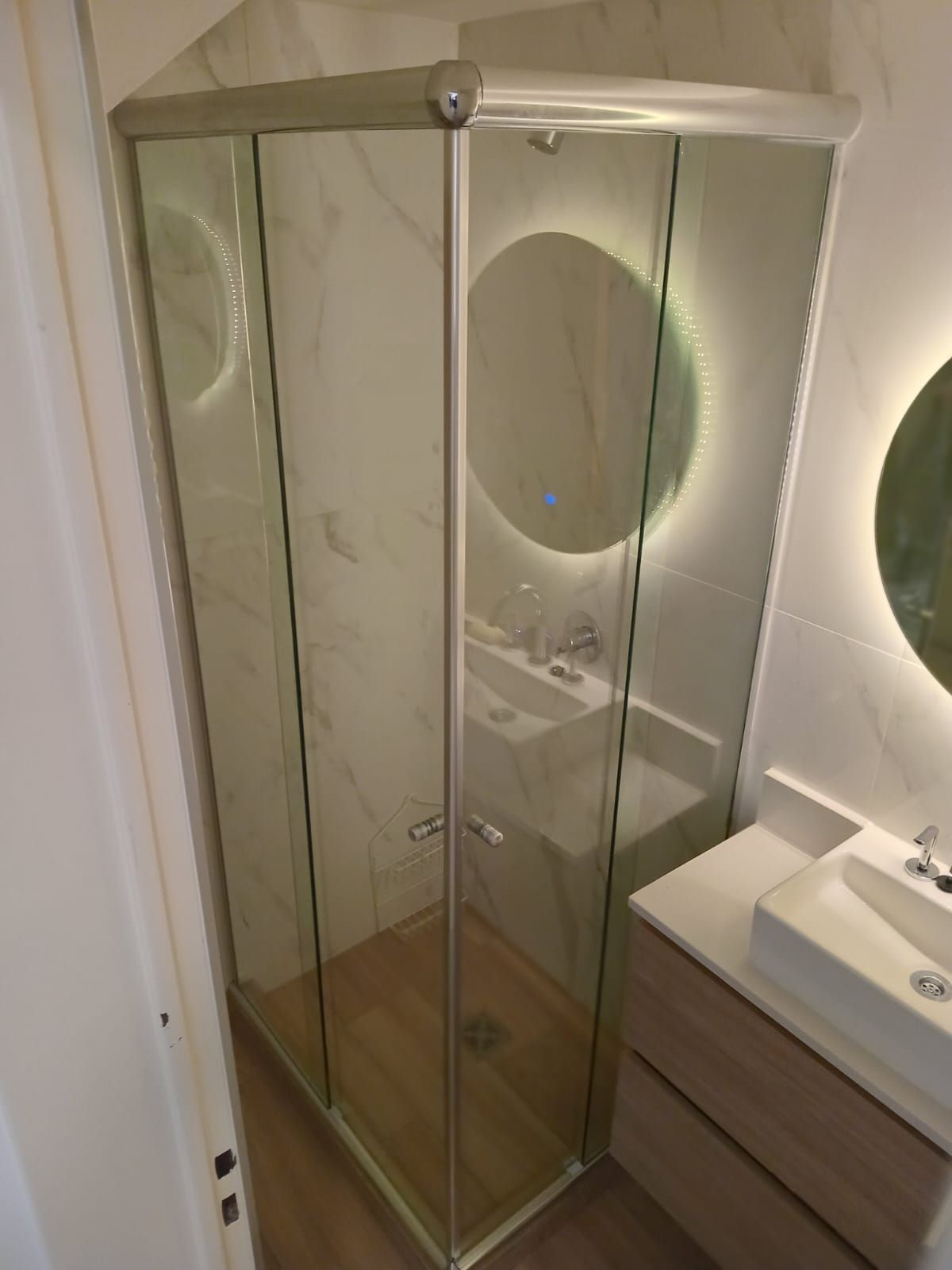 Cabina de ducha de esquina en un baño con lavabo y espejo.