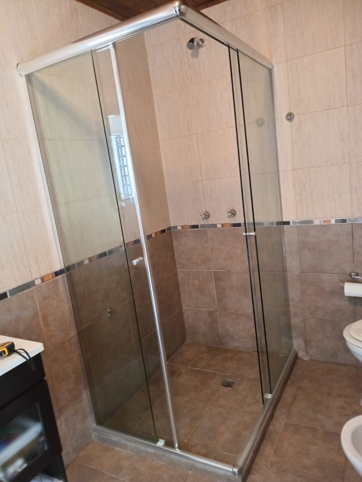 Mampara de ducha de cristal en baño con paredes de azulejos beige y WC.