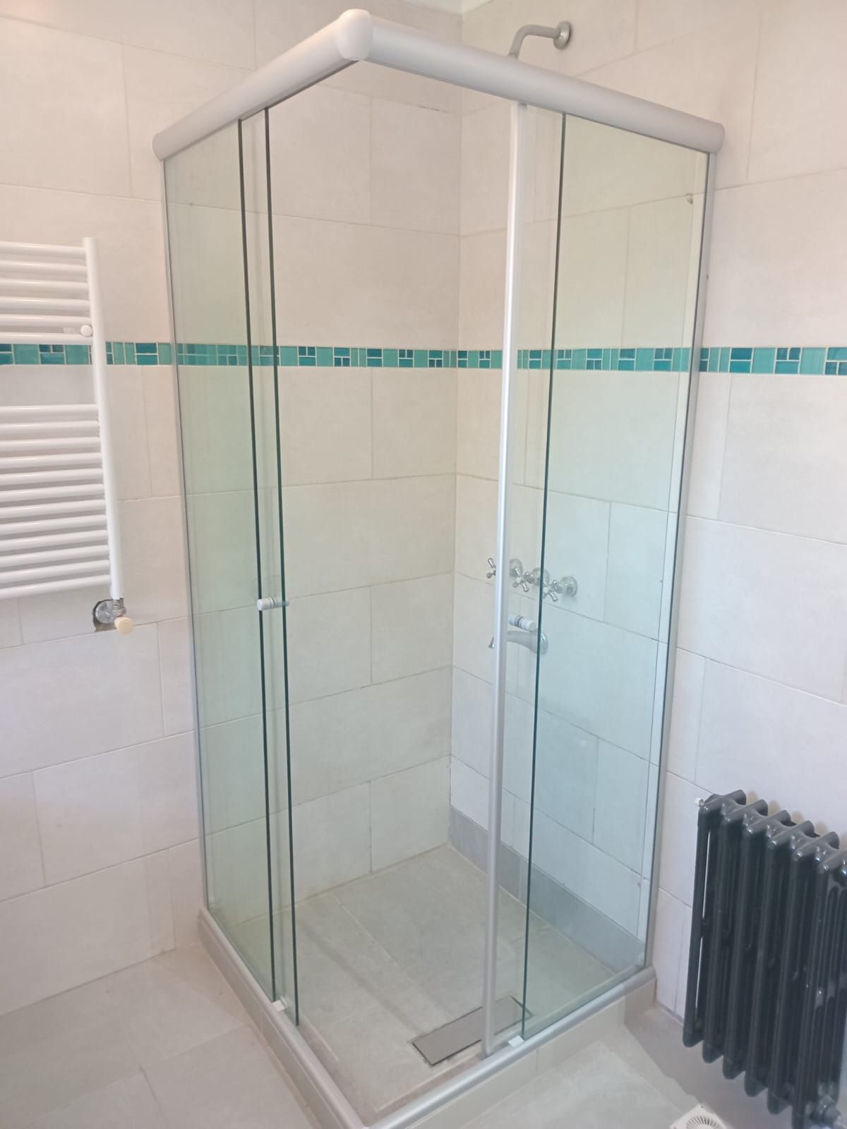 Mampara de ducha de cristal en baño alicatado con toallero y radiador.