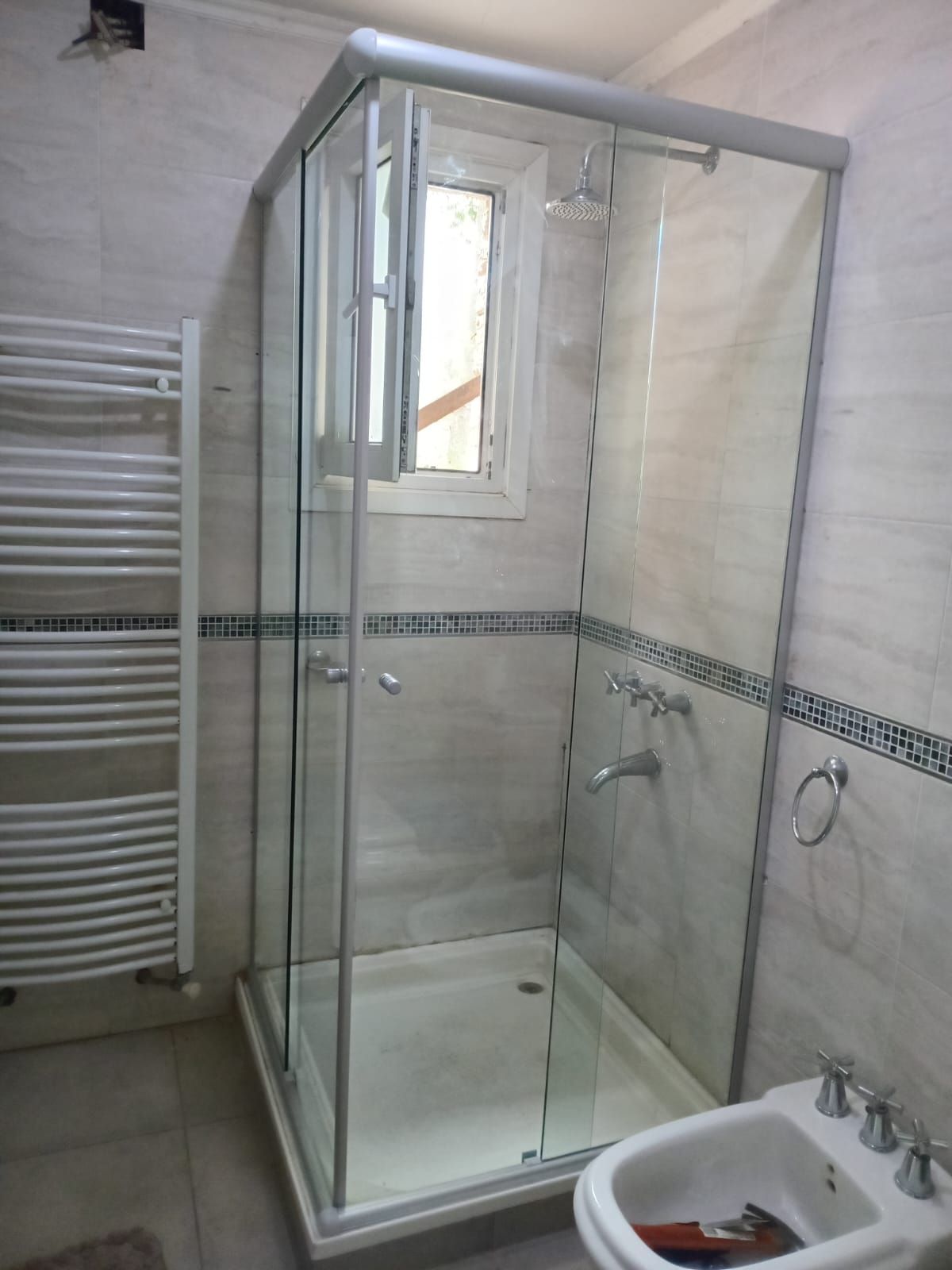 Mampara de ducha de esquina con puertas de cristal en baño con ventana.