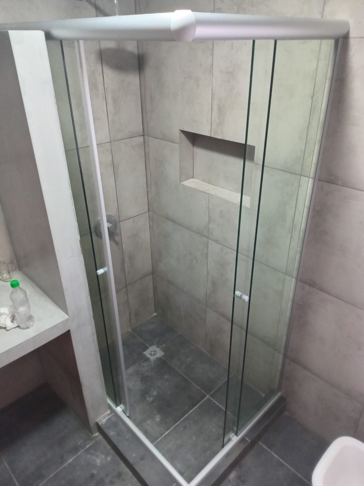 Mampara de ducha de cristal con paredes revestidas de azulejos grises y estante incorporado.