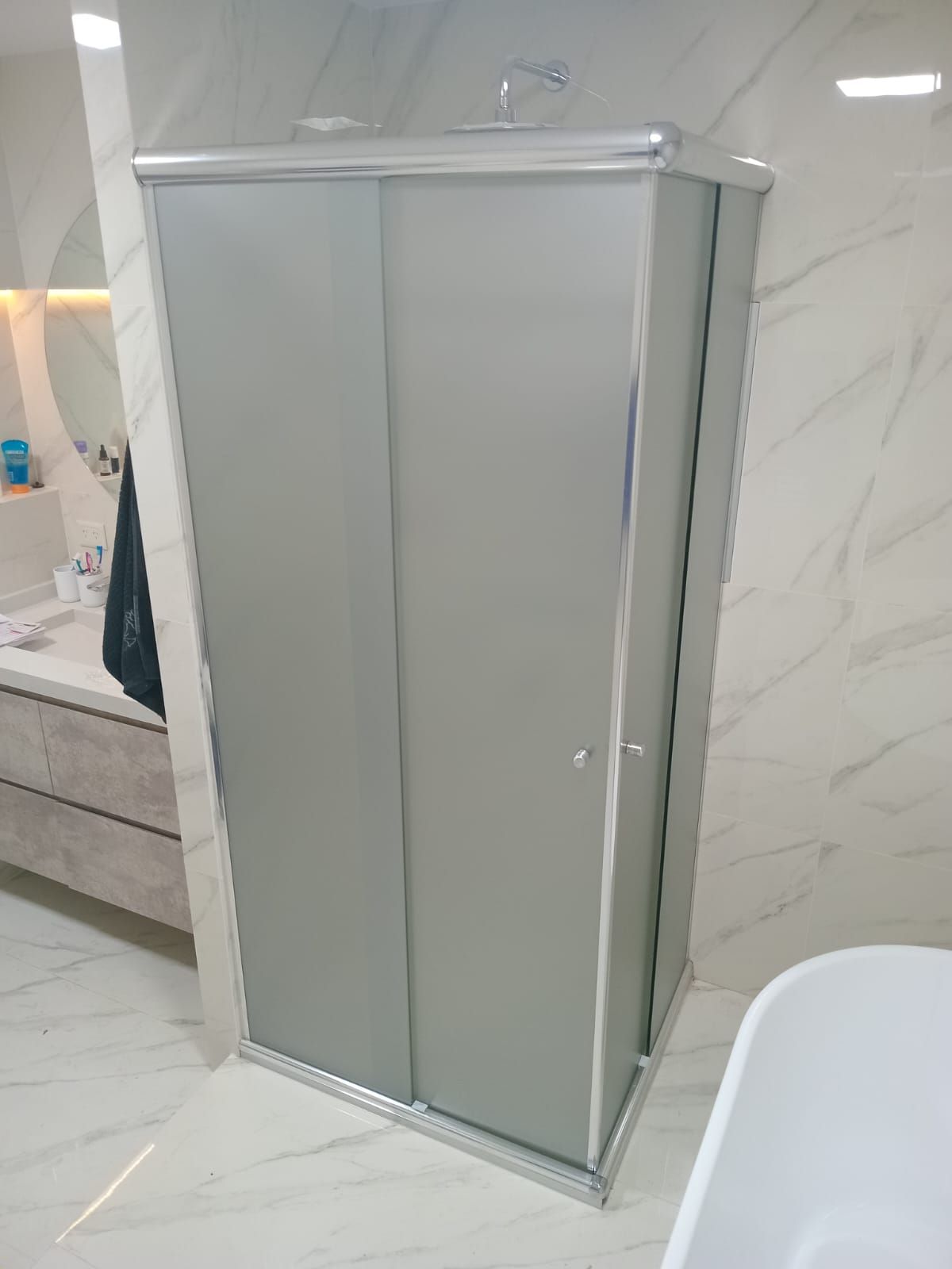 Mampara de ducha de cristal esmerilado gris con puertas correderas en un baño moderno.