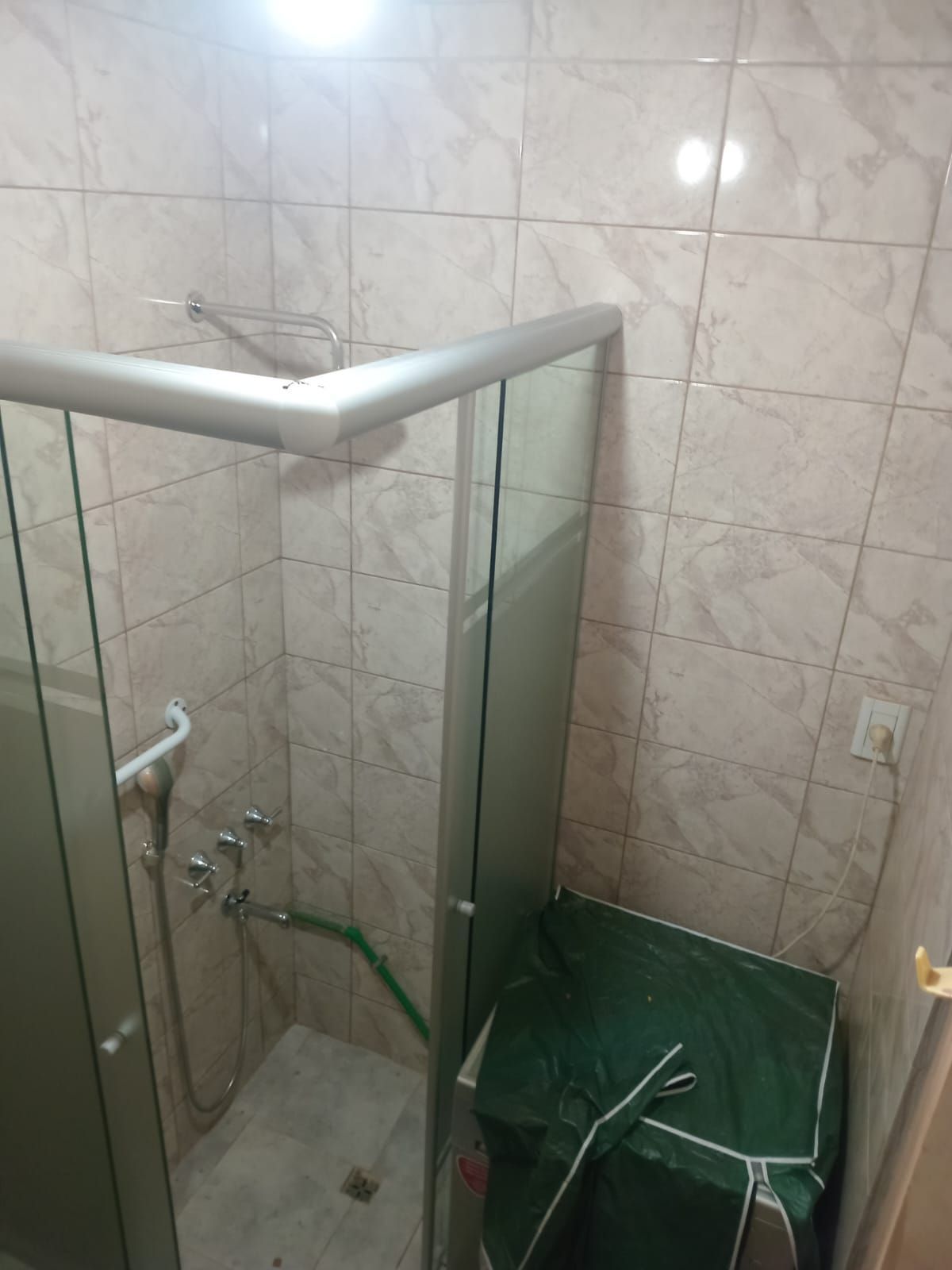 Cabina de ducha con puertas de cristal, marco plateado, paredes de azulejos de color claro