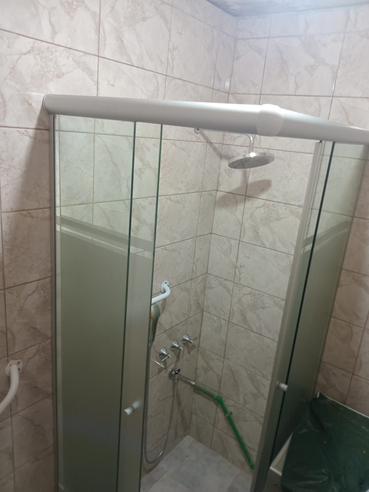 Cabina de ducha con puertas de cristal y cabezal de ducha en un baño alicatado.