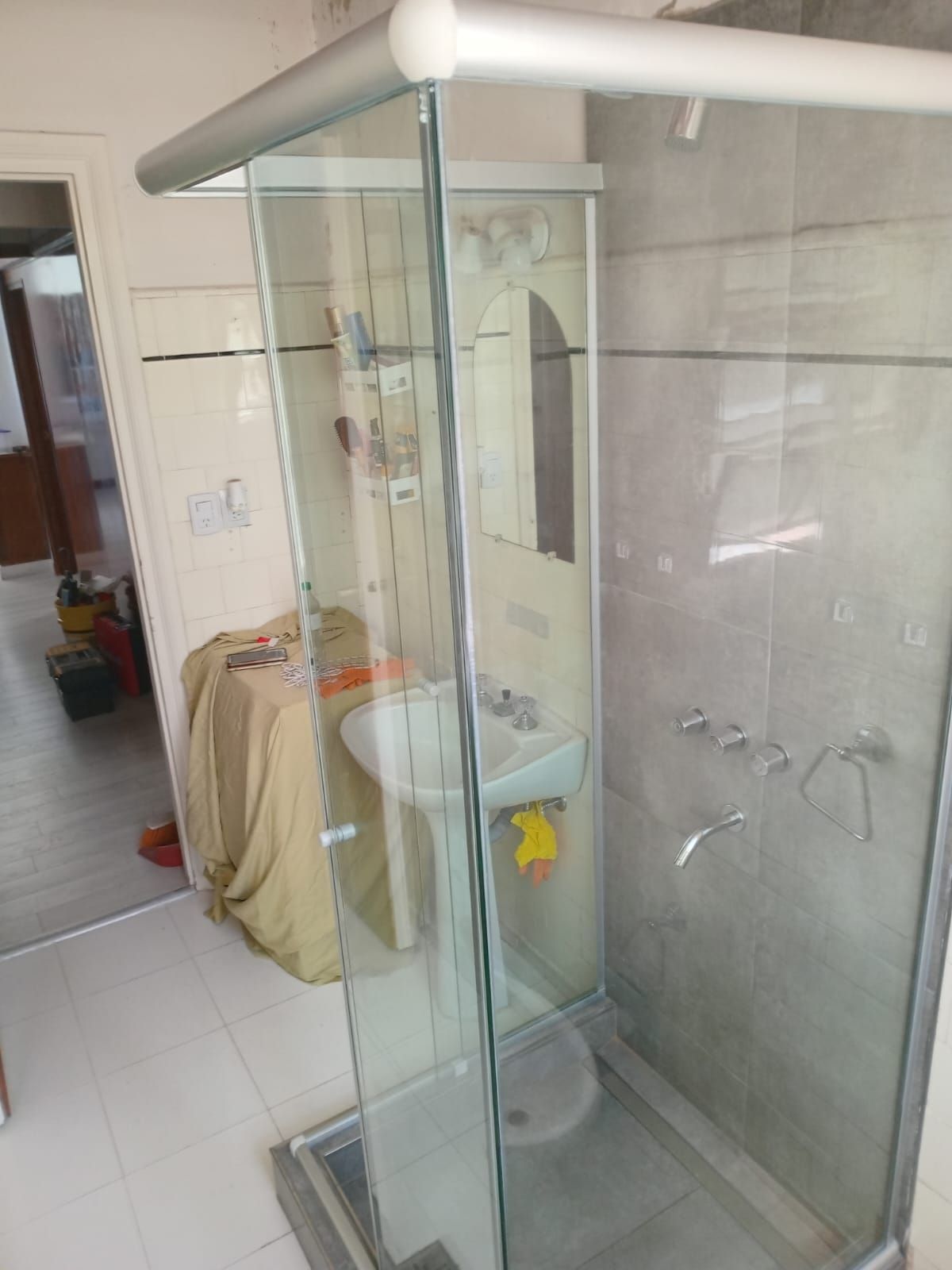 Baño con ducha de cristal, lavabo con pedestal y paredes revestidas de azulejos.