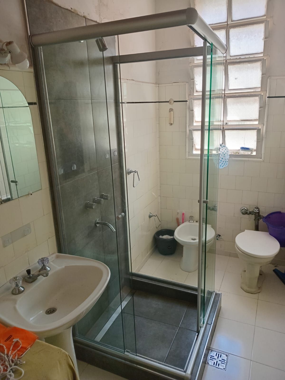 Baño con ducha de cristal, lavabo, inodoro y bidé. Luminoso, con una combinación de colores blanco y gris.