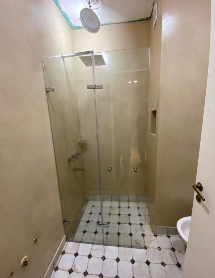 Una ducha moderna con puertas de cristal transparente y un cabezal de ducha cuadrado tipo lluvia.