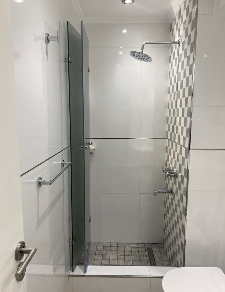 Ducha con puertas de cristal y pared con azulejos a cuadros. Tonos blancos y grises.