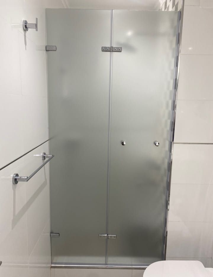 Puerta de ducha de vidrio esmerilado en un baño de azulejos blancos, con herrajes cromados.