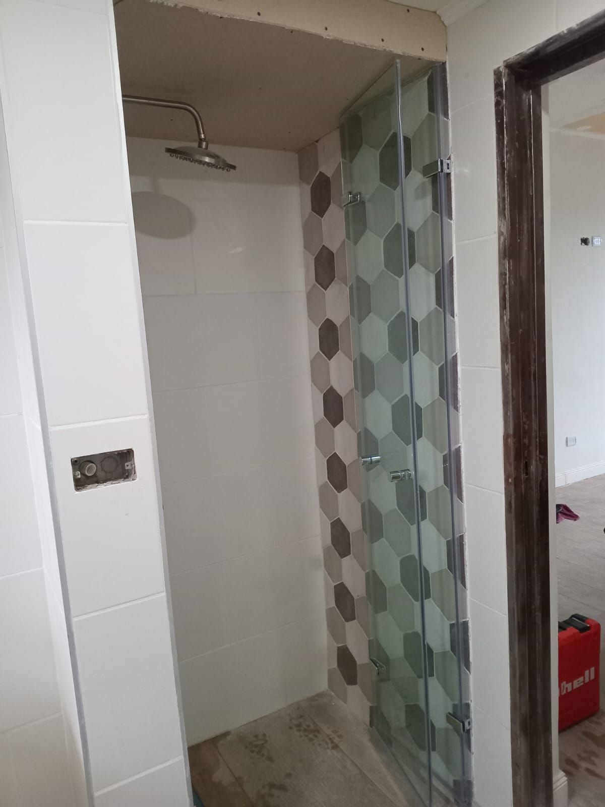 Cabina de ducha con puerta de cristal y pared de azulejos estampados. Paredes blancas a la izquierda